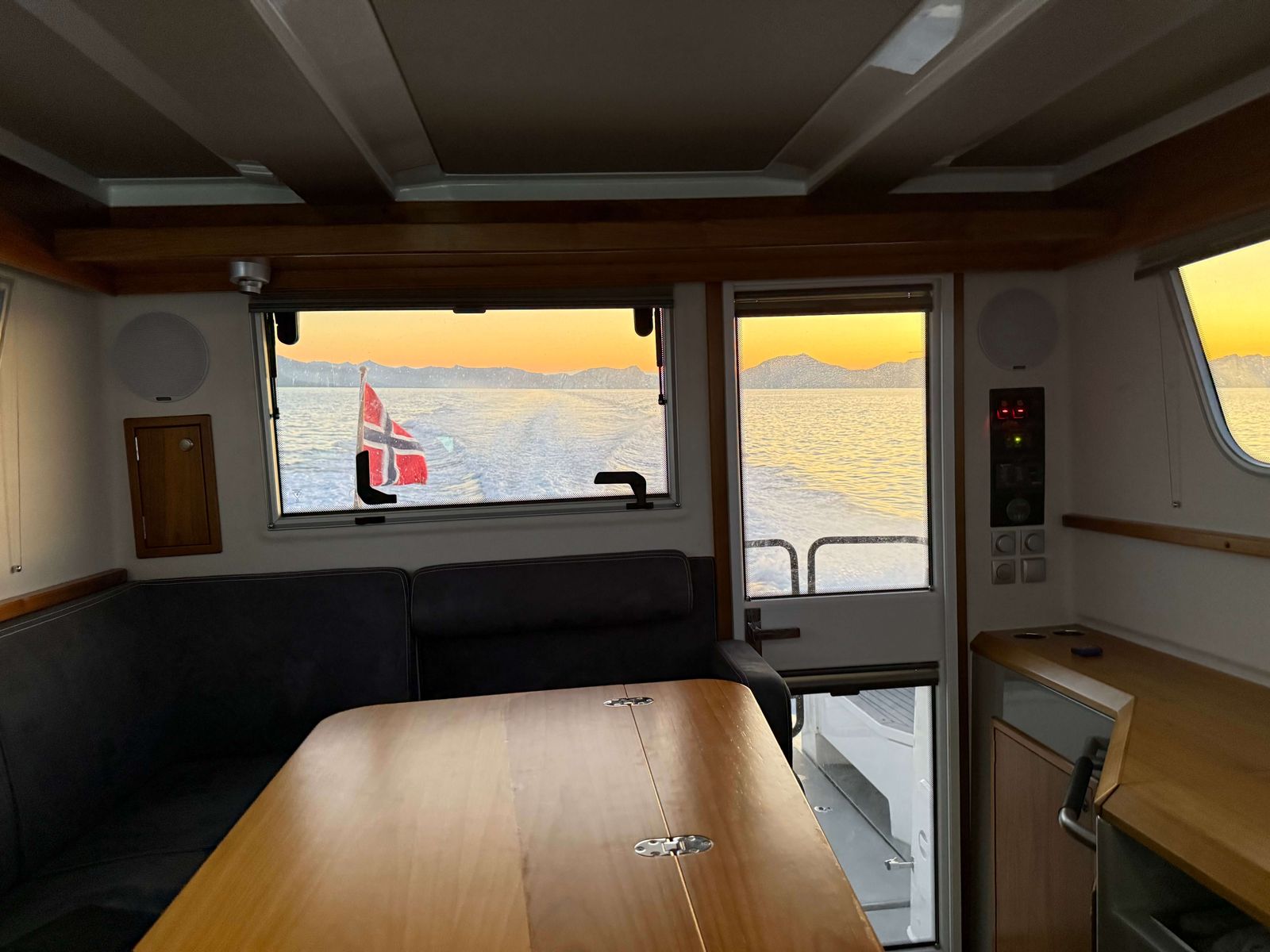 Salongen om bord med bord, benk og panoramavindu mot fjorden