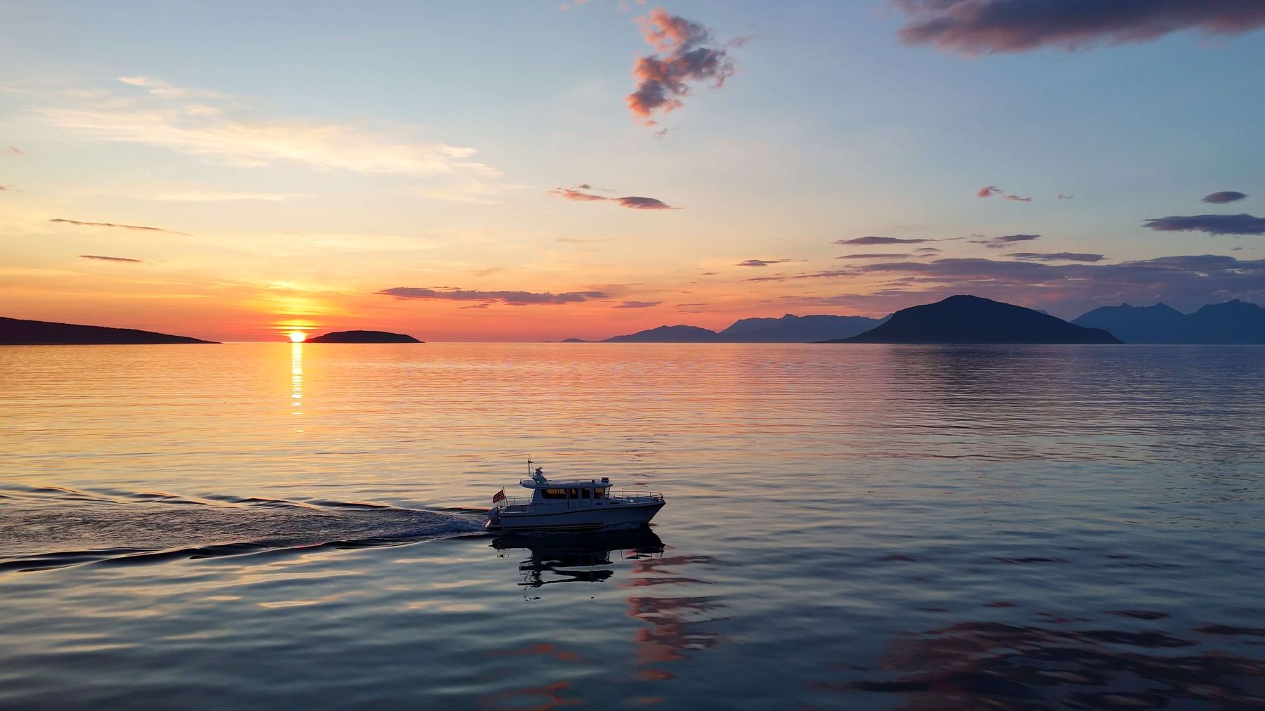 Midnattssol over stille fjord med båt i horisonten